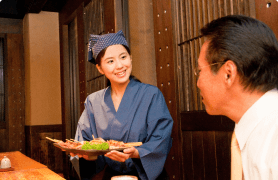 和食居酒屋で笑顔で料理を提供する女性スタッフ